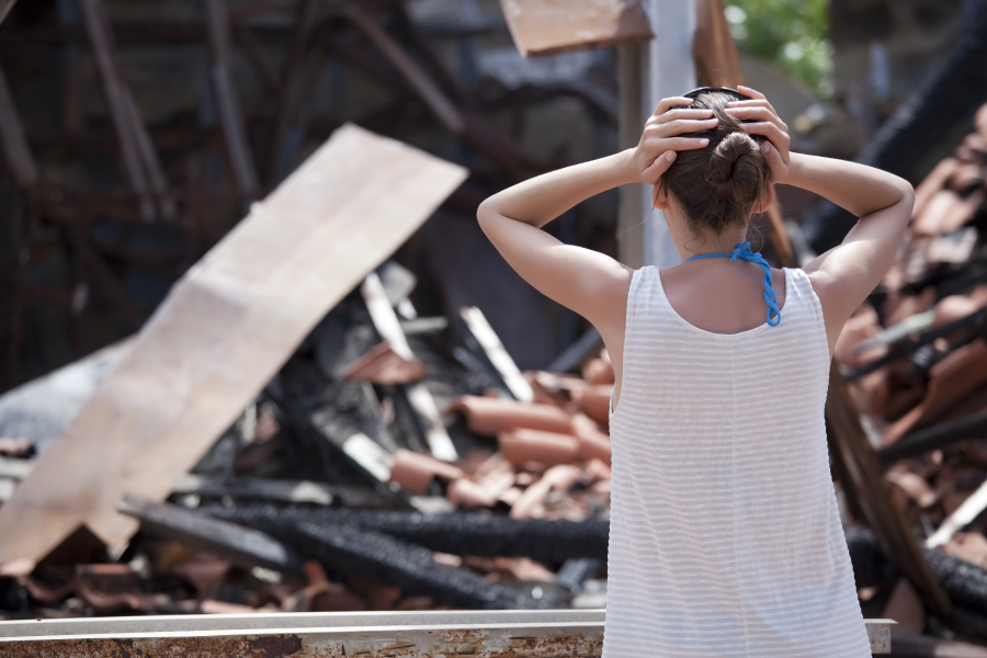 woman standing in front of burned out house and holding her head with both hands